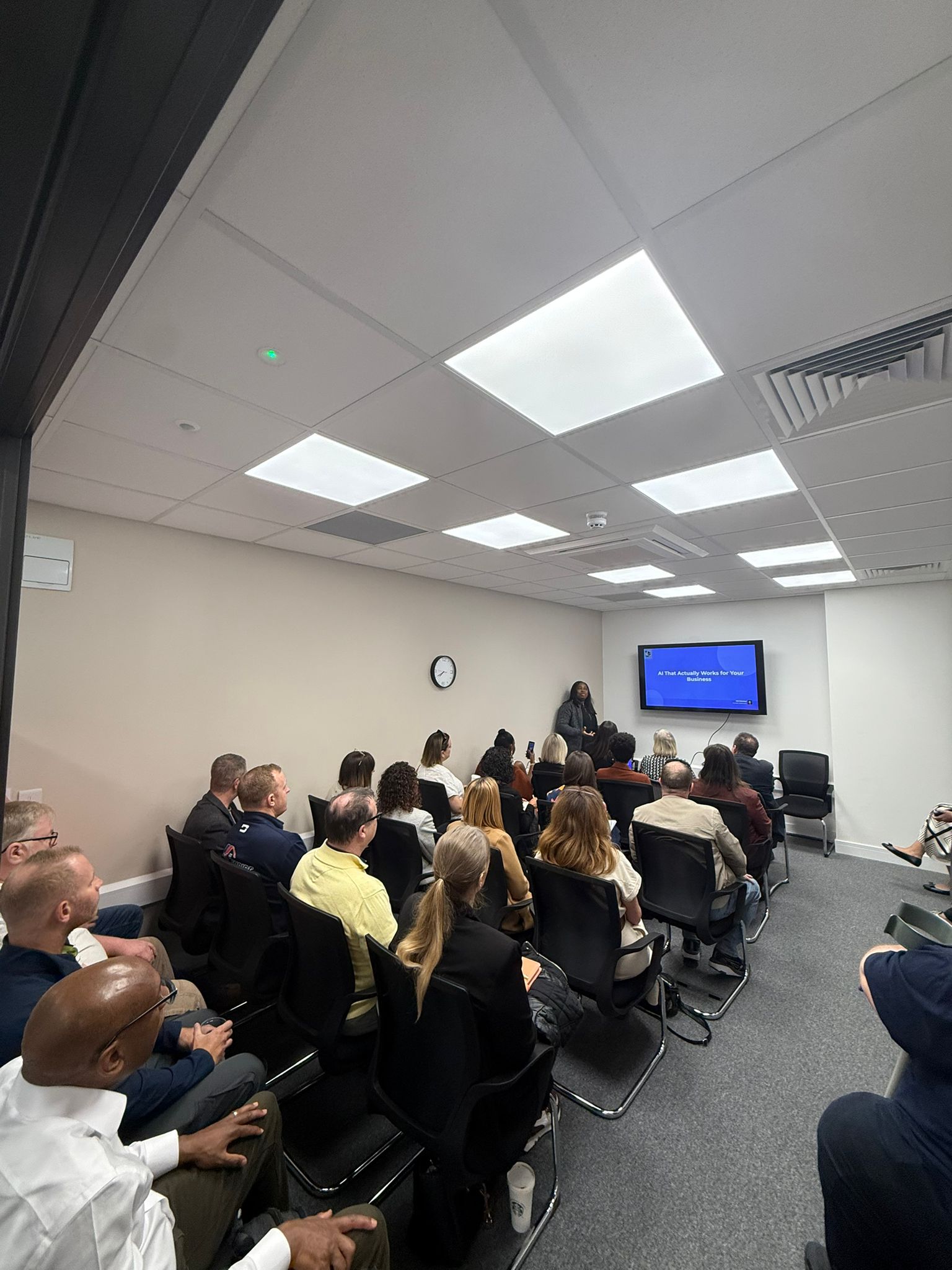 Abi Odedeyi speaking to a packed room, slide reading AI That Actually Works for Your Business